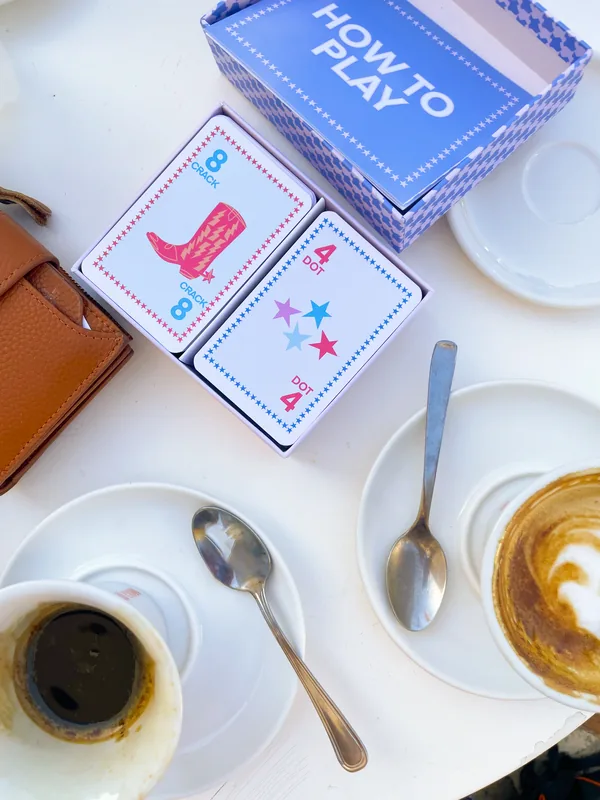 A How to Play box open beside two espresso cups on a café table
