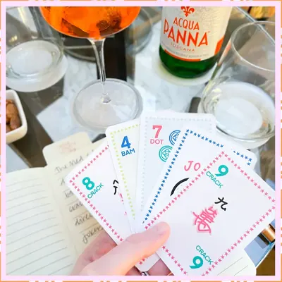 A hand of Classic Edition cards held over a bar table with a spritz, sparkling water and a notebook