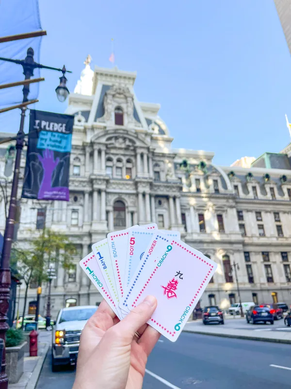 A hand fanning Classic Edition cards in front of Philadelphia City Hall