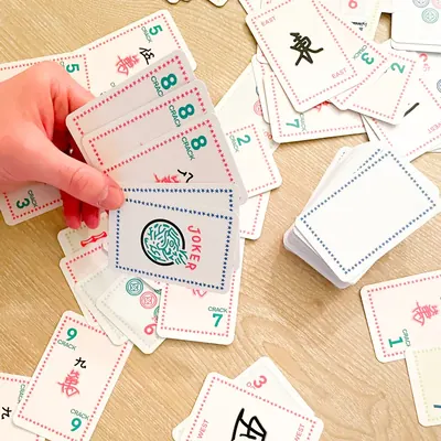 A hand picking a Joker from a scatter of Classic Edition cards on a wood table