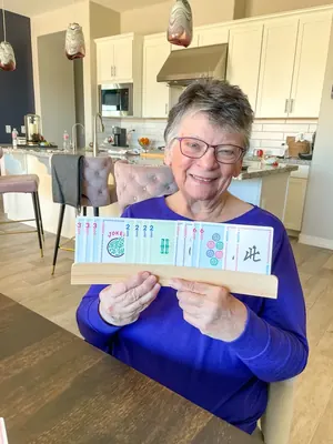 A smiling woman at her kitchen table holding a wooden rack lined with Play Away cards