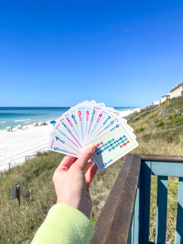 A green knit sleeve holding a fan of Play Away cards over a white-sand beach